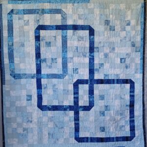 Fiber art print with interlocking square patterns in light and dark blue fabric tones.