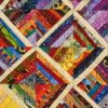 Fiber art quilt with multicolored fabric diamonds arranged in a rhythmic pattern framed with blue and cream borders.