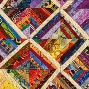 Fiber art quilt with multicolored fabric diamonds arranged in a rhythmic pattern framed with blue and cream borders.