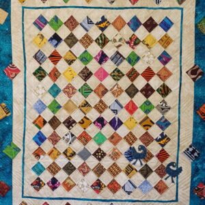 Fiber art quilt with colorful diamond grid patterns framed by blue and patterned fabric borders.