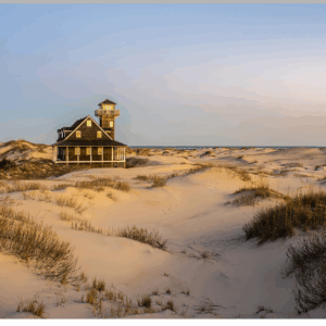 Photograph of Oregon Inlet Life Saving Station surrounded by sandy dunes at sunset.