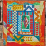 Brightly colored fiber art quilt with geometric blocks, checkerboard squares, and a bold central red motif.