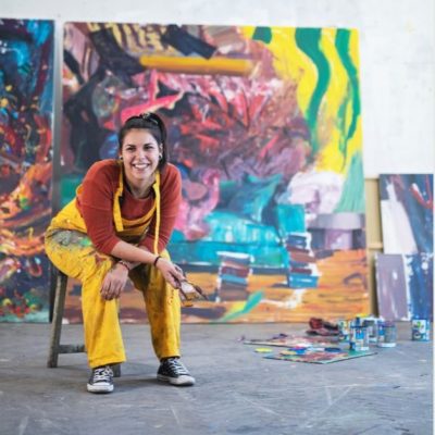A close-up of well-used paintbrushes in a container, illuminated by soft, colorful bokeh lights in the background.
